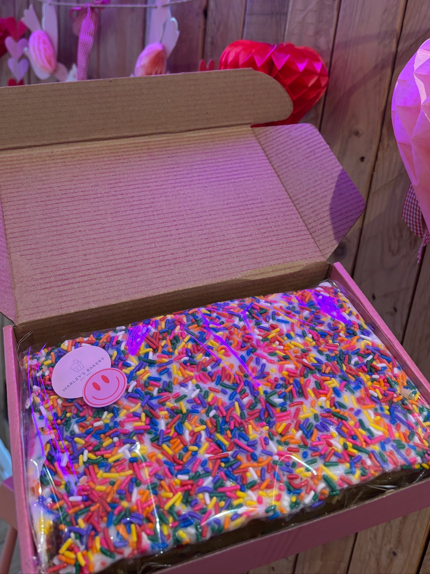 Gluten free old school cake topped with white icing and colourful sprinkles in gift box